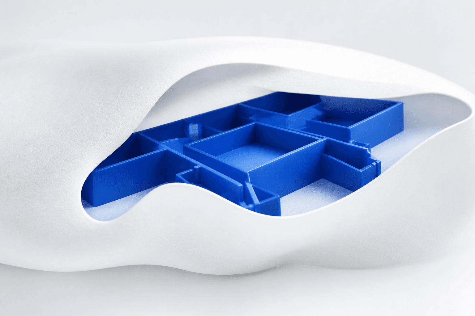 A white sculptural shell reveals an ordered cobalt-blue modular system within.